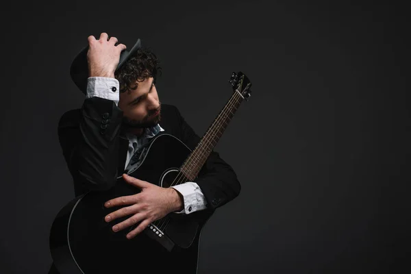 Beau musicien en chapeau embrassant sa guitare sur noir — Photo de stock