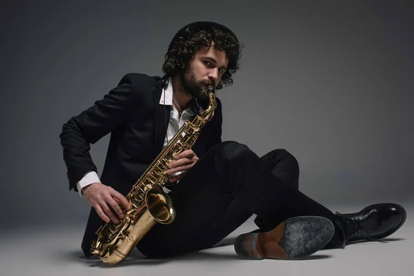 Jazzman barbu jouant du saxophone assis sur le sol — Photo de stock