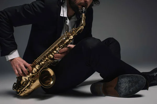 Tiro recortado de músico tocando saxofone enquanto sentado no chão — Fotografia de Stock