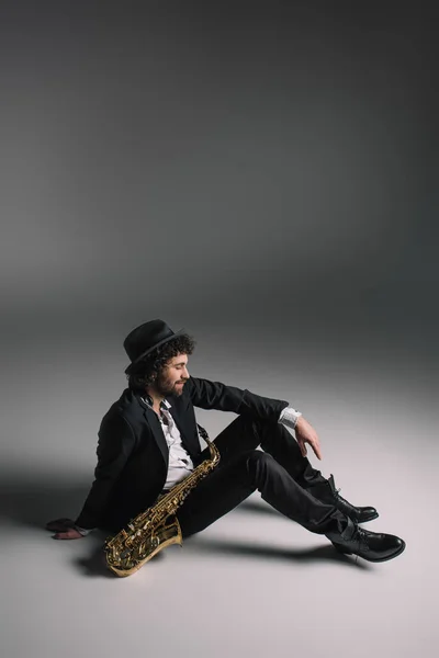 Красивий музикант сидить на підлозі з саксофоном — стокове фото