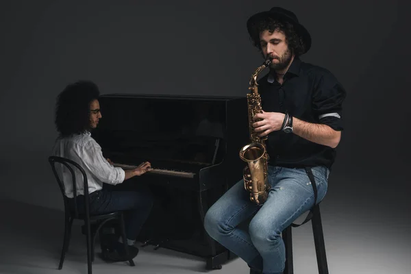 Homem tocando saxofone enquanto seu parceiro tocando piano embaçado no fundo — Fotografia de Stock