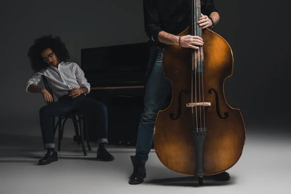 Cortado tiro de homem tocando violoncelo enquanto seu parceiro deprimido sentado no piano borrado no fundo — Fotografia de Stock