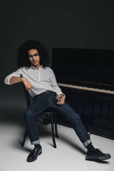 Guapo músico elegante con vaso de whisky delante del piano - foto de stock