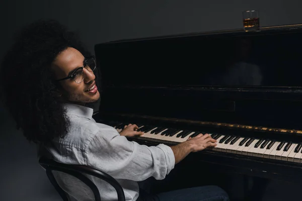 Lächelnder junger Musiker spielt Klavier auf schwarz — Stockfoto