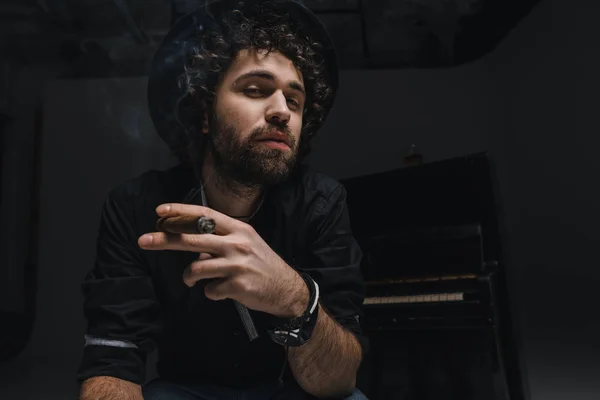 Serious musician smoking cigar in front of piano on black — Stock Photo