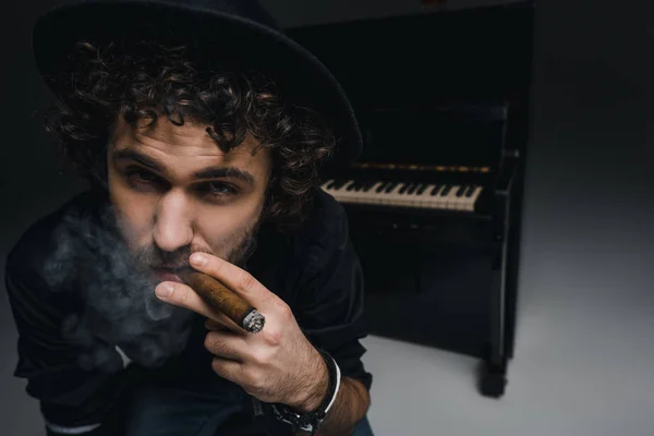 Primer plano retrato de un joven músico fumando cigarro delante del piano y mirando a la cámara - foto de stock