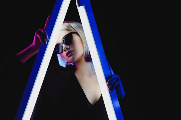 Stylish girl posing in sunglasses with two ultra violet lamps, isolated on black — Stock Photo