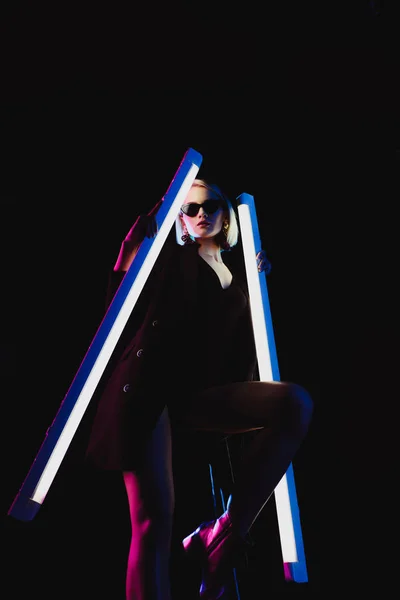 Stylish model posing with two ultra violet lamps for fashion shoot, isolated on black — Stock Photo