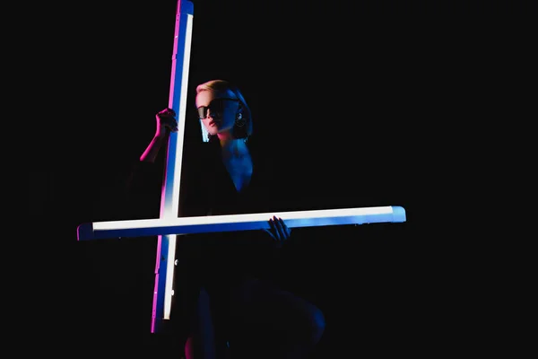 Стильная молодая девушка позирует с двумя ультрафиолетовыми лампами для моды съемки, изолированные на черном — стоковое фото