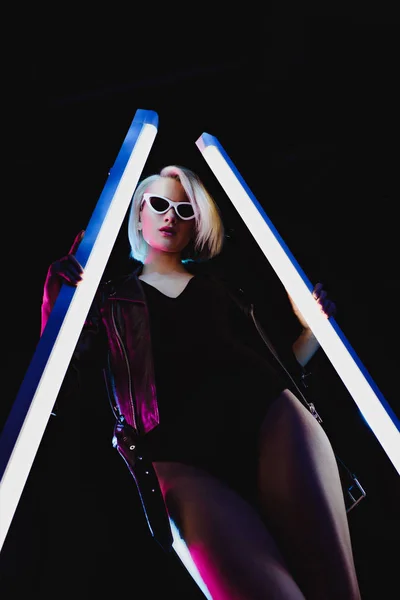 Красивая стильная девушка позирует с двумя ультрафиолетовыми лампами, изолированными на черном — стоковое фото