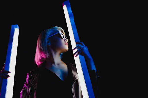 Beau modèle élégant posant avec deux lampes ultraviolettes pour le tournage de mode, isolé sur noir — Photo de stock