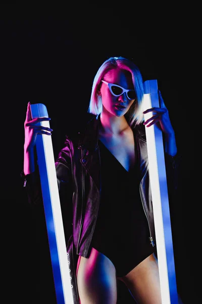 Ragazza alla moda posa in occhiali da sole con due lampade ultraviolette, isolato su nero — Foto stock