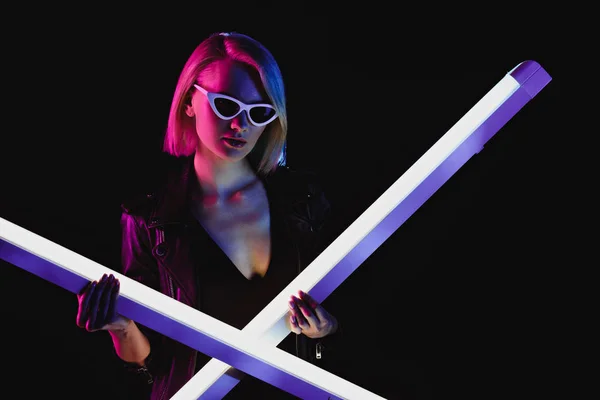 Модна дівчина в сонцезахисних окулярах позує з двома ультрафіолетовими лампами, ізольовані на чорному — стокове фото