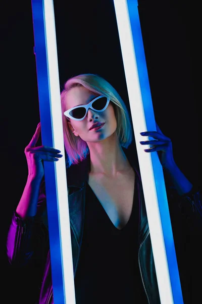 Sonriente chica de moda posando con dos lámparas ultravioleta, aislado en negro - foto de stock