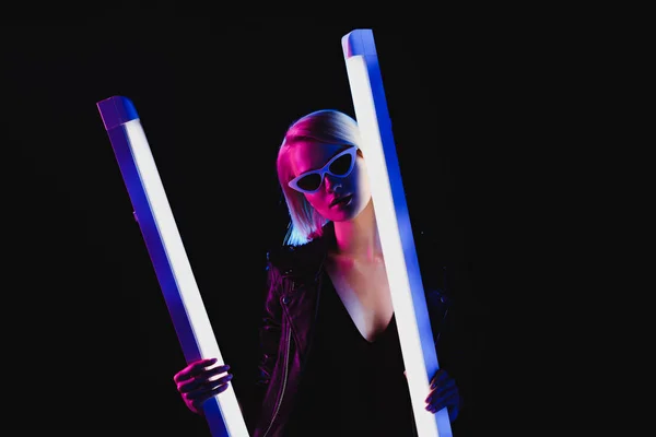 Стильная девушка позирует с двумя ультрафиолетовыми лампами, изолированными на черном — стоковое фото