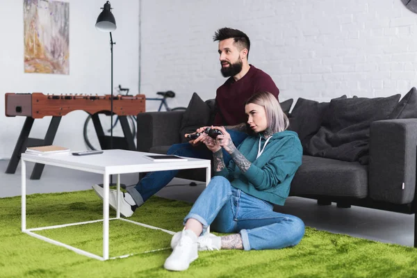 Pareja tatuada jugando videojuego en la sala de estar - foto de stock