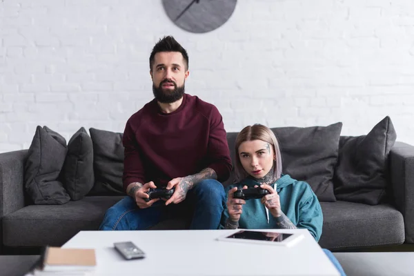 Seria pareja tatuada jugando videojuego en casa - foto de stock