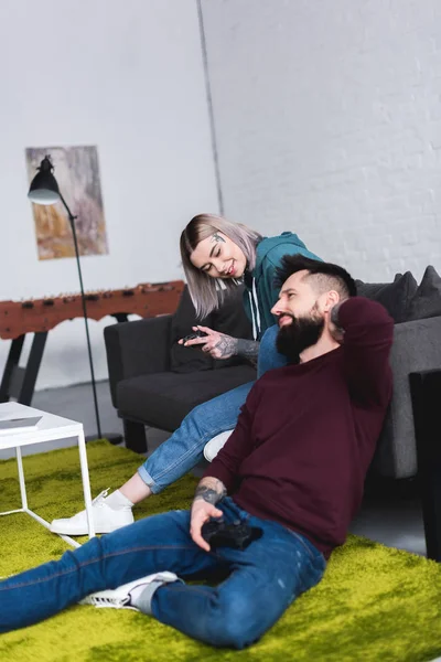 Pareja tatuada jugando videojuego en la sala de estar - foto de stock