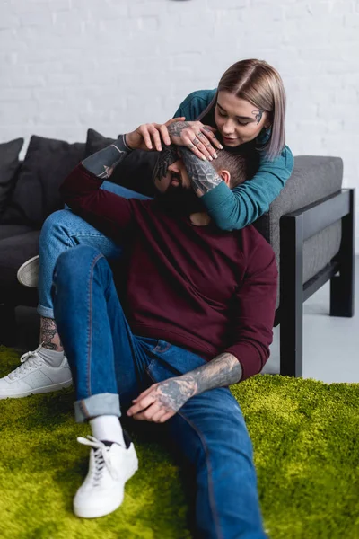 Feliz tatuado novia cubriendo novios ojos en sala de estar - foto de stock