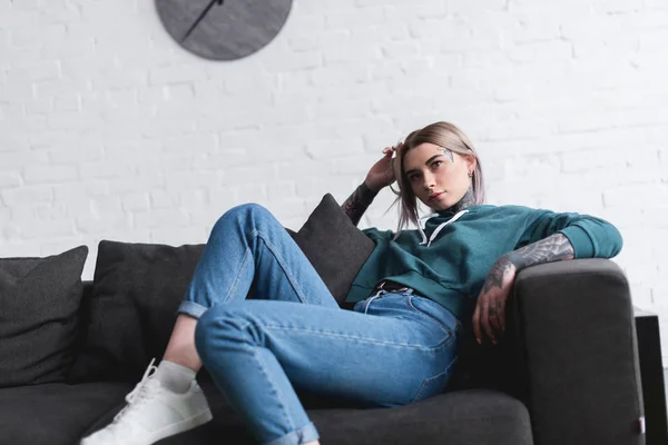 Beautiful tattooed girl sitting on sofa and looking away — Stock Photo