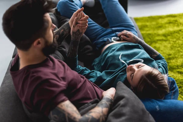 Татуированная пара, лежащая на диване и держащаяся за руки — стоковое фото