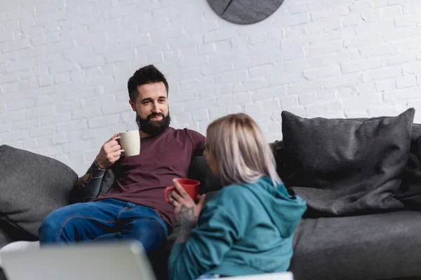 Pareja tatuada bebiendo café y mirándose en casa - foto de stock