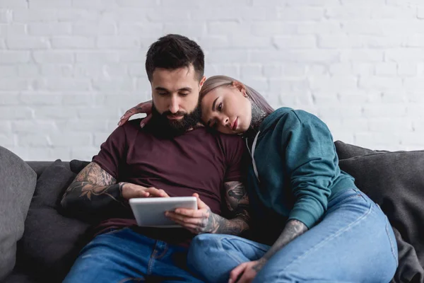 Tattooed couple watching something at tablet at home — Stock Photo