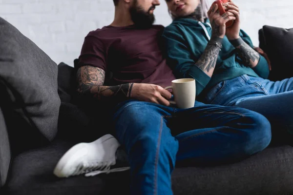 Cropped image of tattooed couple drinking coffee at home — Stock Photo