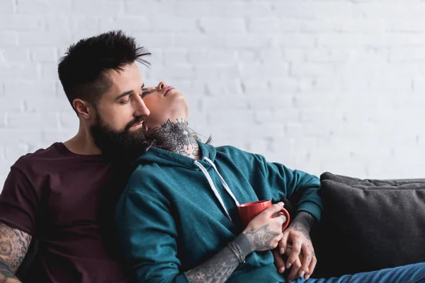 Casal tatuado sentado no sofá com xícara de café — Fotografia de Stock