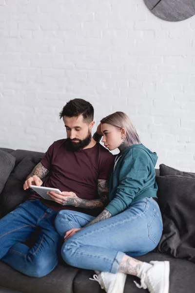 Casal tatuado olhando para tablet no sofá na sala de estar — Fotografia de Stock