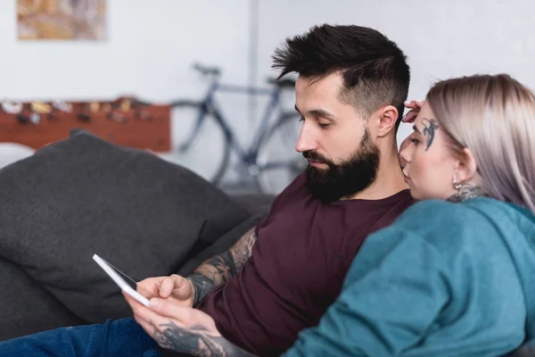 Tätowiertes Paar schaut zu Hause auf dem Sofa auf Tablet — Stockfoto