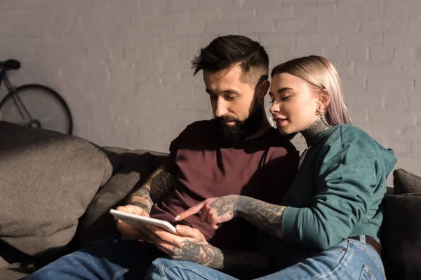 Tattooed girlfriend pointing on something at tablet to boyfriend — Stock Photo
