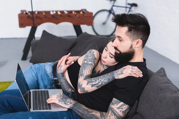 Vista laterale della coppia tatuata guardando il computer portatile a casa — Foto stock