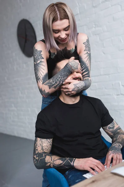 Татуированная девушка прикрыла глаза парням, пока он работал за компьютером. — стоковое фото