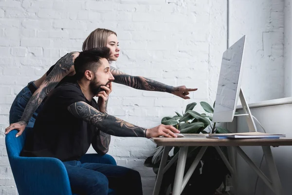 Tattooed girlfriend pointing on something at computer to boyfriend — Stock Photo