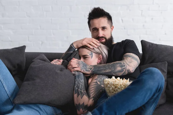 Tattooed couple watching horror movie on sofa at home — Stock Photo