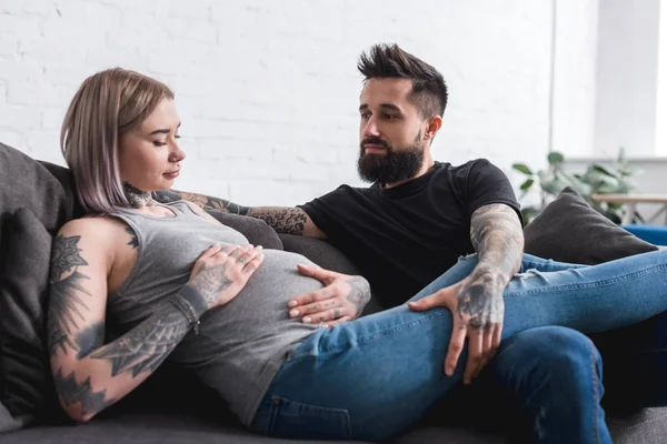 Tatoué enceinte copine toucher l'abdomen près de copain à la maison — Photo de stock