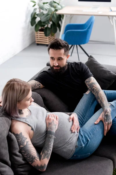 Tattooed pregnant girlfriend lying on sofa with boyfriend — Stock Photo