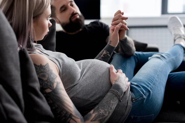 Embarazada tatuado novia y novio cogido de la mano en casa - foto de stock