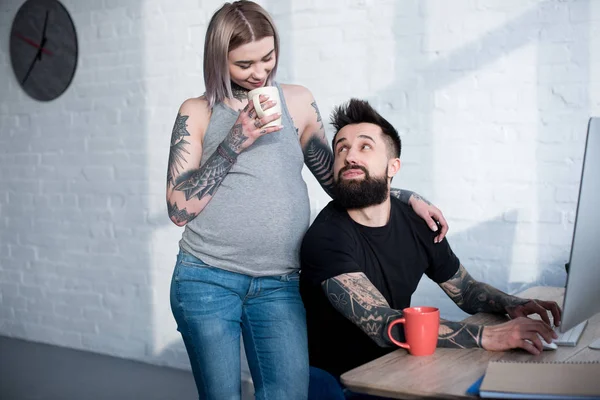 Tatuado grávida namorada beber chá e abraçar namorado em casa — Fotografia de Stock