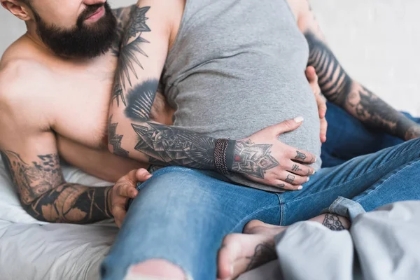 Abgeschnittenes Bild von Freund umarmt schwangere tätowierte Freundin auf dem Bett — Stockfoto