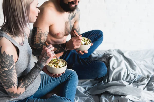 Cropped image of pregnant tattooed girlfriend eating salad with shirtless boyfriend — Stock Photo