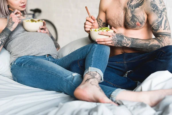 Cropped image of pregnant tattooed girlfriend eating salad with boyfriend at home — Stock Photo