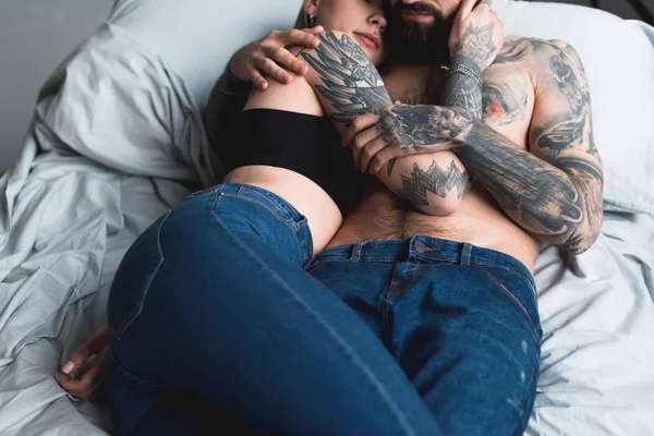 Imagen recortada de pareja tatuada abrazándose y acostada en la cama - foto de stock