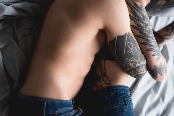 Cropped image of tattooed couple hugging on bed — Stock Photo