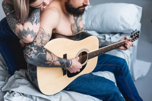 Обрезанный образ татуированного бойфренда, играющего на гитаре для подружки дома — стоковое фото