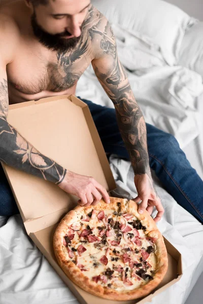 Sem camisa bonito tatuado homem com pizza na cama — Fotografia de Stock