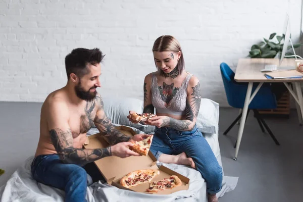Tattooed couple eating pizza on bed — Stock Photo