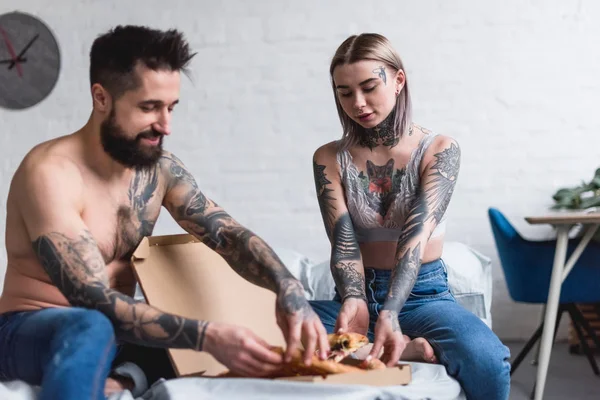 Casal tatuado tomando pizza na cama em casa — Fotografia de Stock