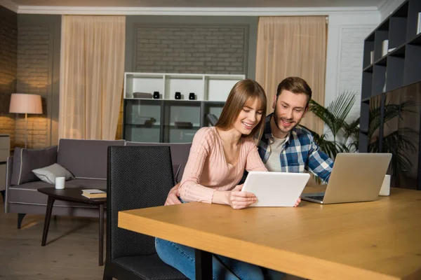 Pareja feliz en la mesa con ordenador portátil y tableta digital en la sala de estar con diseño interior - foto de stock